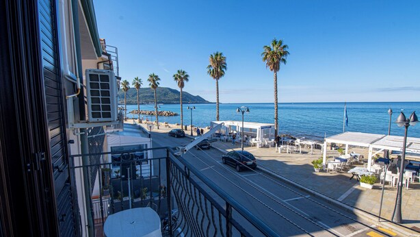 A balcony with a view of a coastal street, palm trees, and a clear blue sky. - Terrazza sul mare (Santa Maria di Castellabate)