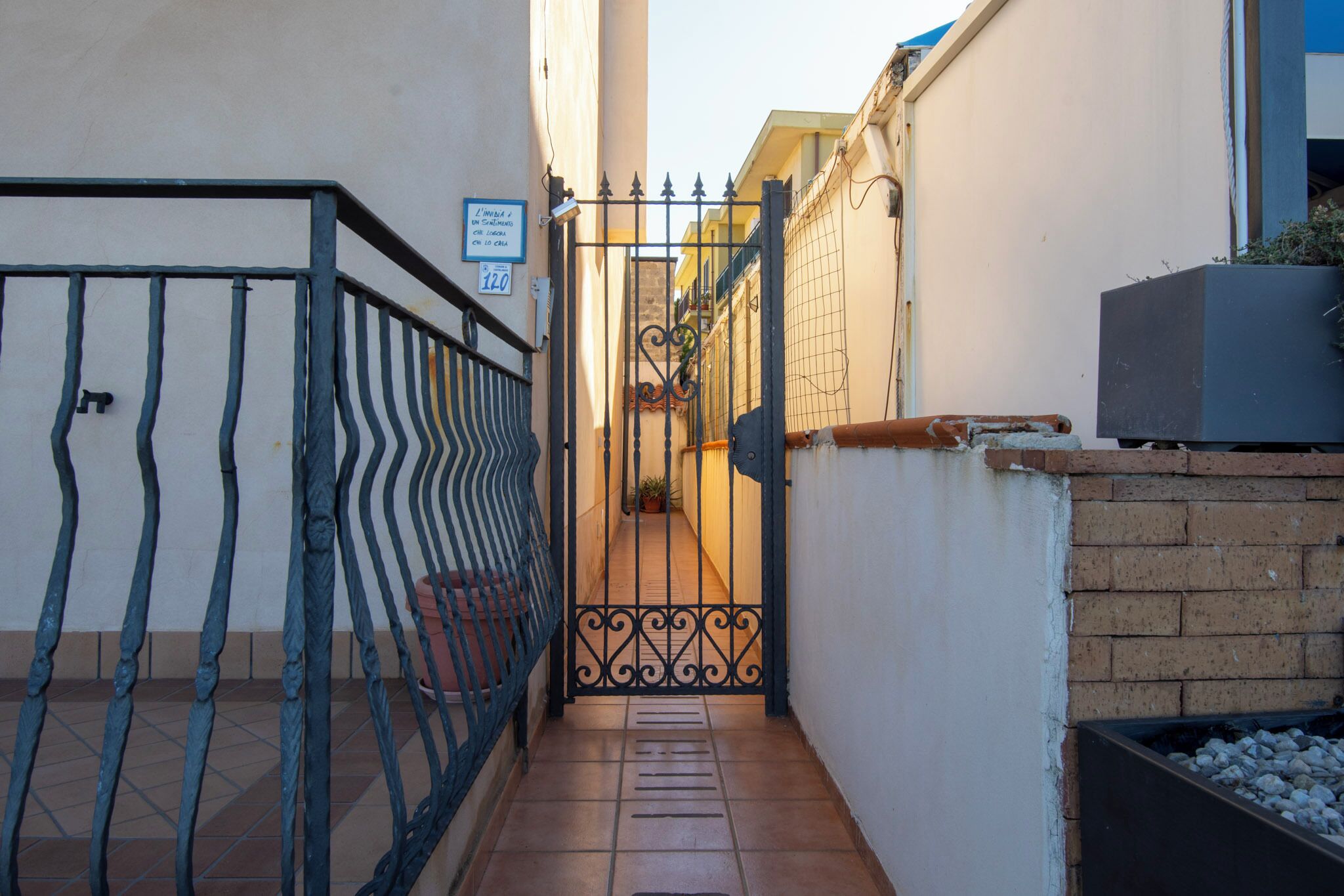 Une ruelle étroite, avec un portail en métal, un sol carrelé et un mur de briques.