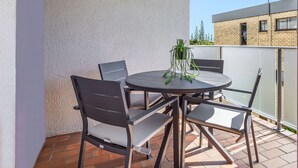 A patio with a round table and four chairs, a potted plant, and a view of a building in the background. - Cosy 2-bedroom Seaside Unit Steps From Beach (Sunshine Coast)