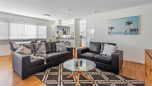 A modern living room with two black leather sofas, a glass coffee table, and a patterned rug. - Cosy 2-bedroom Seaside Unit Steps From Beach (Sunshine Coast)