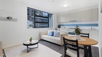 A modern kitchen with white cabinets, a dining table with chairs, a small round table with a plant, and a sofa with blue cushions.