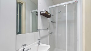 Un baño con lavamanos blanco, un espejo y una ducha con mampara de vidrio.