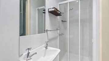A bathroom with a white sink, a mirror, and a glass-enclosed shower.