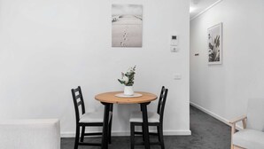 Un comedor con una mesa redonda de madera, dos sillas negras y un jarrón blanco con flores.
