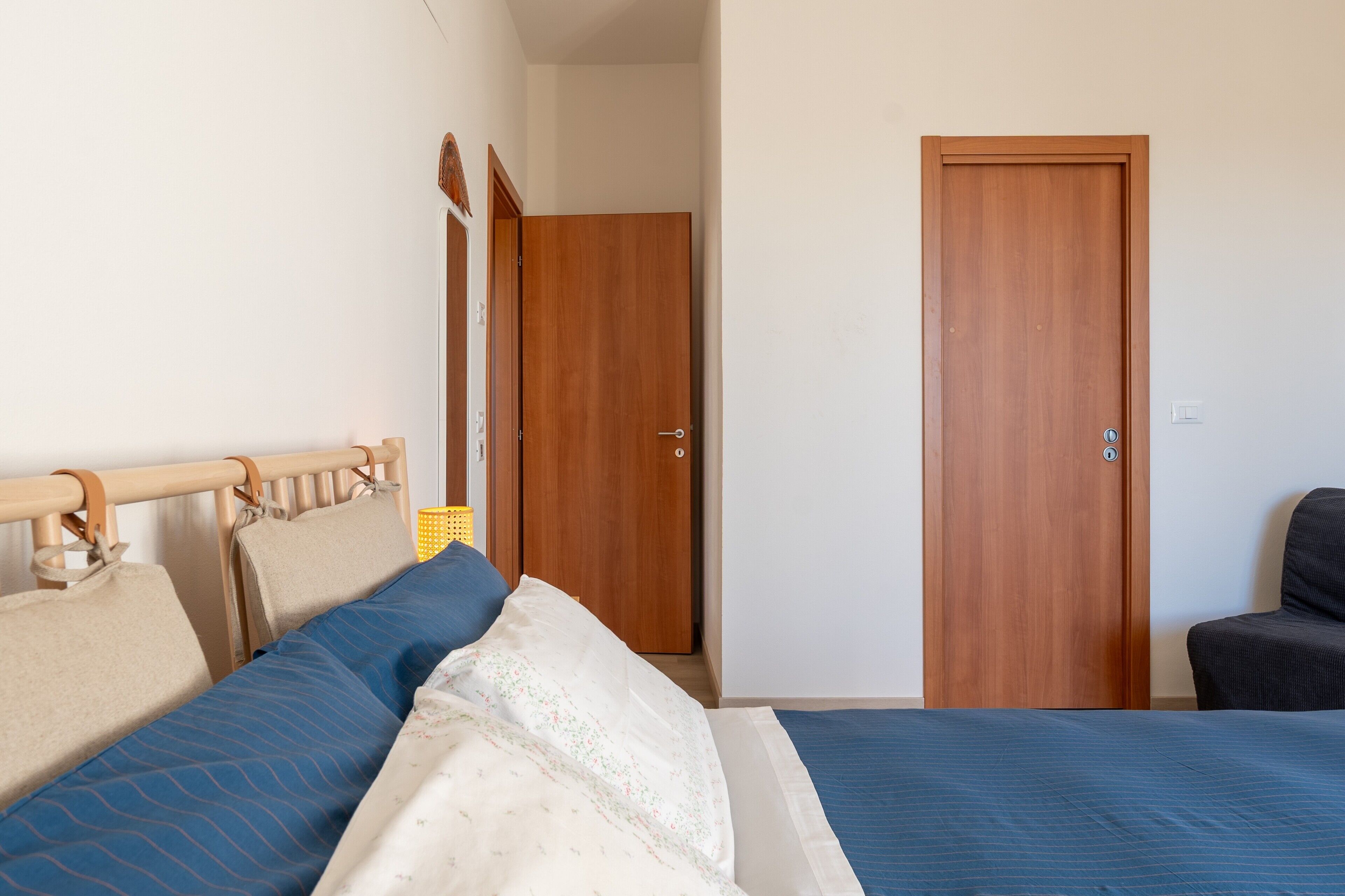 A bedroom with a bed, two wooden doors, a chair, and a bedside table.