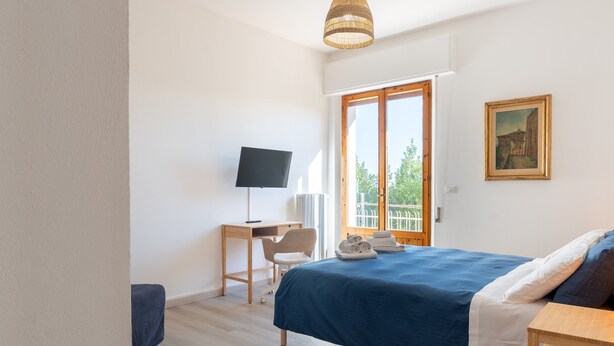 Ein Schlafzimmer mit Bett, Schreibtisch, Stuhl, Fernseher und einem Fenster mit Aussicht.