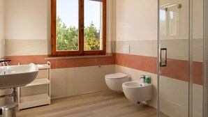 Ein Badezimmer mit Waschbecken, Toilette, Bidet und einem Fenster mit Blick auf Bäume.
