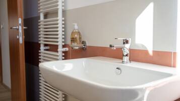 A bathroom with a white sink, chrome faucet, and a bottle of hand soap on the counter.