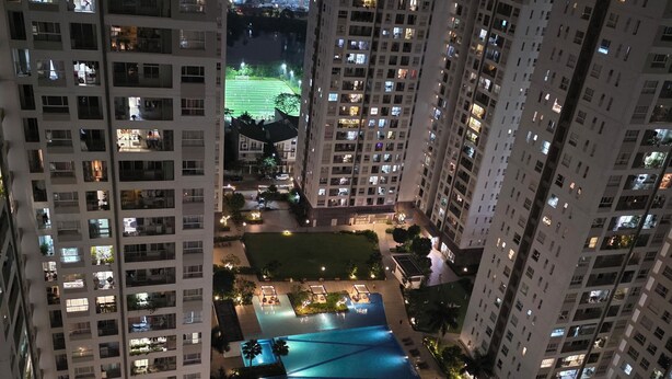 A high-rise residential building with multiple balconies, a rooftop pool area, and a well-lit courtyard.