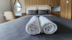 A neatly made bed with rolled towels, a wooden headboard, a small bedside table, and a chair.