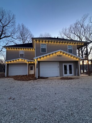 Une maison à deux étages avec un garage, une véranda et des guirlandes lumineuses.