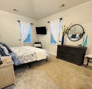 A bedroom with a bed, dresser, TV, and a mirror.