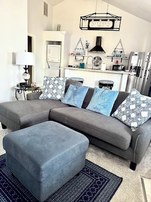 A modern living room with a grey sectional sofa, patterned throw pillows, a small side table, and a blue rug.