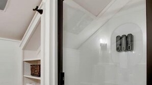 Ein Badezimmer mit Duschkabine aus Glas, weißen Ablagen mit Handtüchern und einem kleinen Fenster.