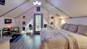 Une chambre comprenant un lit, un bureau et une chaise, une porte donnant sur un espace extérieur et un luminaire fixé au plafond.
