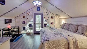 Ein Schlafzimmer mit Bett, Schreibtisch und Stuhl, einer Tür zu einem Außenbereich und einer Deckenleuchte.