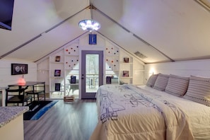 Une chambre comprenant un lit, un bureau et une chaise, une porte donnant sur un espace extérieur et un luminaire fixé au plafond.