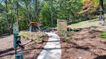 A pathway leading to a pet waste station in a wooded area with a small wooden structure and a bench.