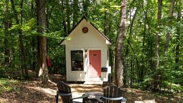 Eine Holzhütte mit roter Tür, umgeben von Bäumen, und zwei Adirondack-Stühlen davor.