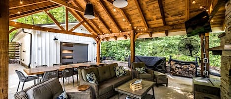 An outdoor covered patio with wooden beams, a dining table, chairs, a sofa, and a fan.