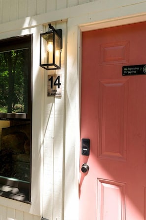 A pink door with a no smoking or vaping sign, a house number 14, and a light fixture above the door.