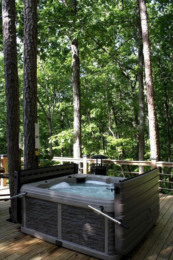 A hot tub on a wooden deck surrounded by trees.