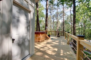 Una terraza de madera con un jacuzzi, rodeada de árboles altos.