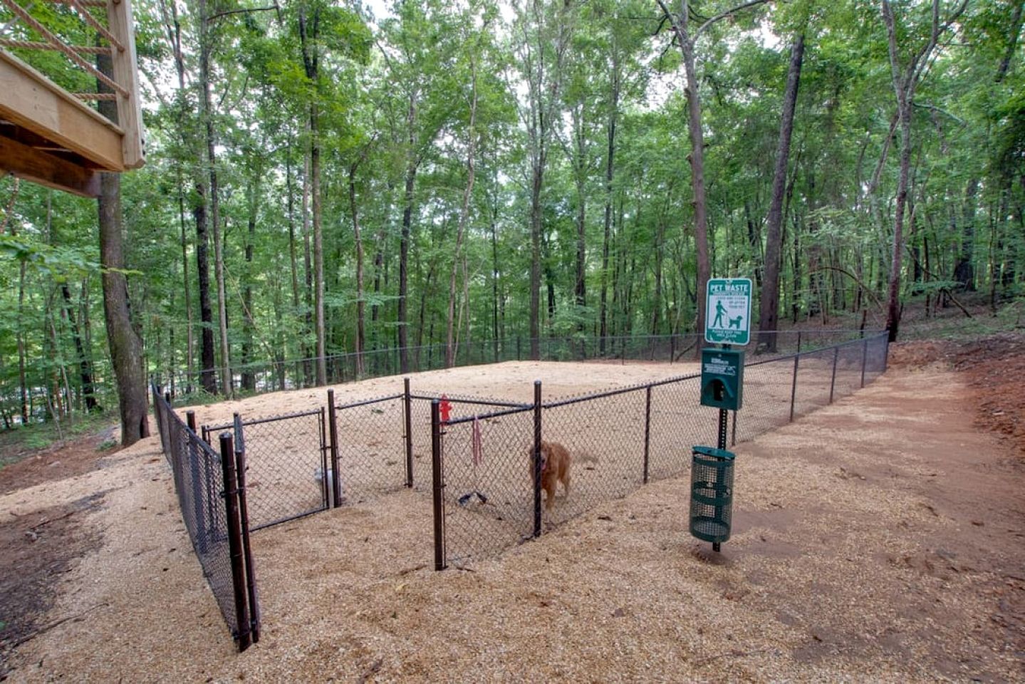 A fenced outdoor area with a pet waste station, surrounded by trees.