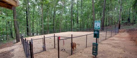 A fenced outdoor area with a pet waste station, surrounded by trees.