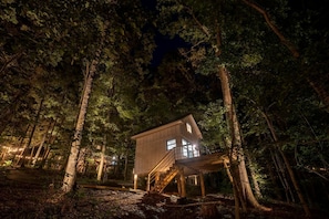 Una cabaña en un bosque con una escalera de madera que lleva a una entrada con ventanas.
