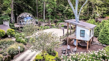 A treehouse with a deck, surrounded by a garden and a dome structure.