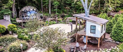 Une cabane dans les arbres dotée d’une terrasse, entourée d’un jardin et d’une structure en forme de dôme.