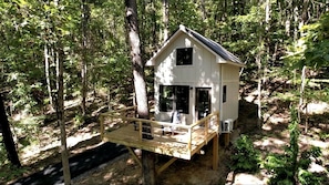 A treehouse with a wooden deck, a small porch, and a single-story structure. - Lofted Romantic Tree House Immersed in Nature in Alabama (Scottsboro)