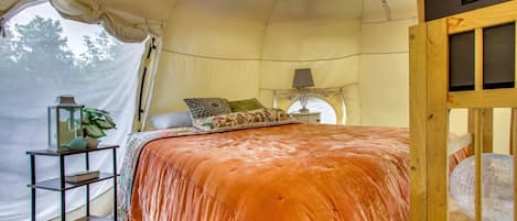 Een tent met een bed, een nachtkastje, een lamp en een plankje met een plant erop.