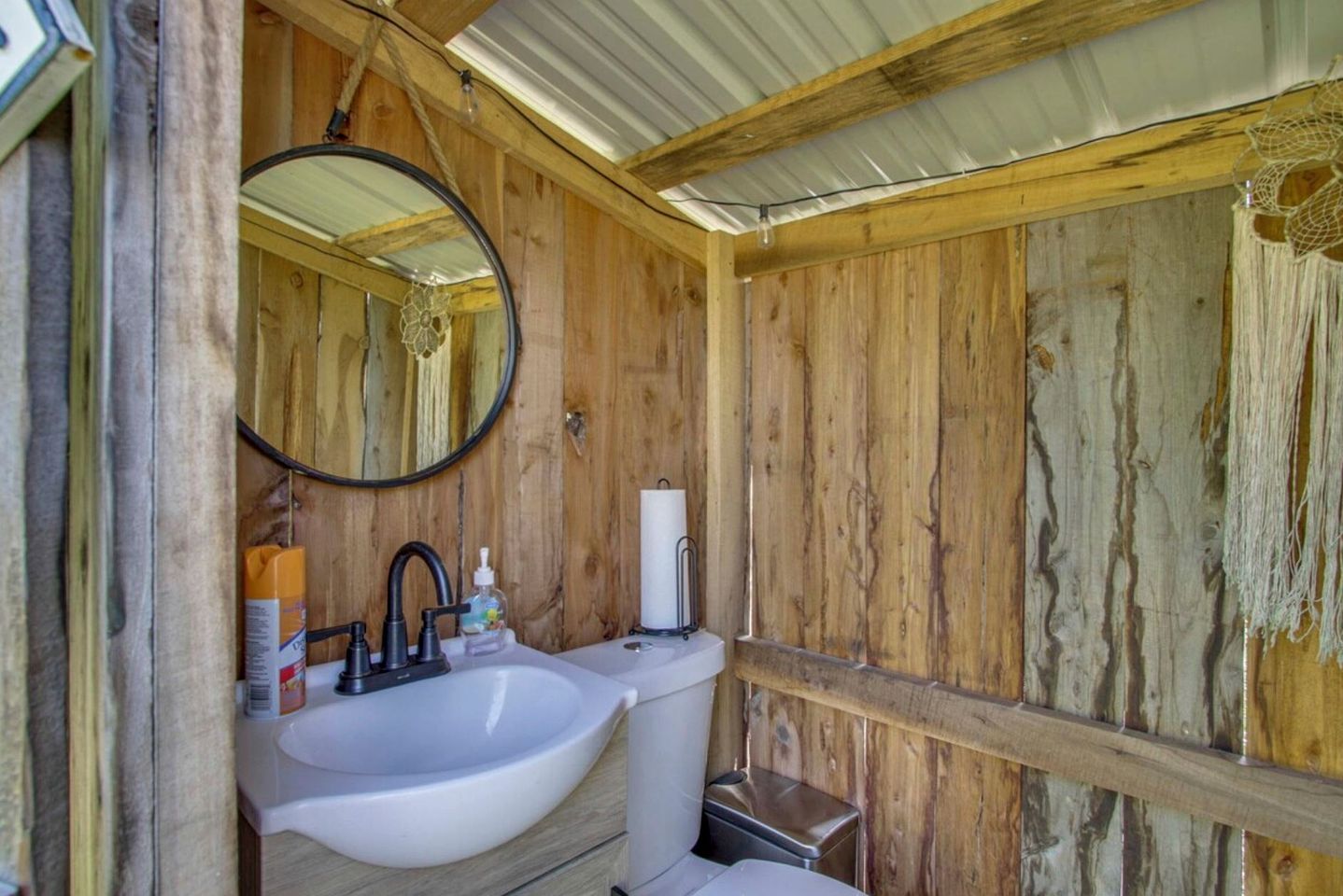 Een rustieke badkamer met houten inrichting, een ronde spiegel, een wit wastafelmeubel en een toilet.