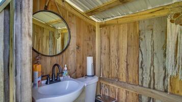 Een rustieke badkamer met houten inrichting, een ronde spiegel, een wit wastafelmeubel en een toilet.