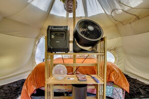 A tent interior with a bed, a speaker, a fan, a globe, and a table with a book and a remote control.