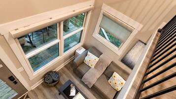 A high-ceilinged room with a staircase, large windows, and a seating area with a coffee table.