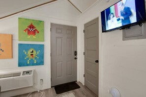 Un couloir avec une porte grise, un téléviseur fixé au mur et une œuvre d’art en pixels sur le mur.