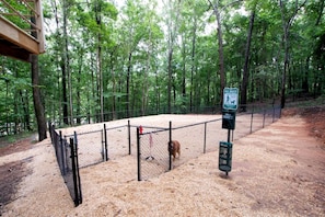 A fenced outdoor area with a pet waste station, surrounded by trees.