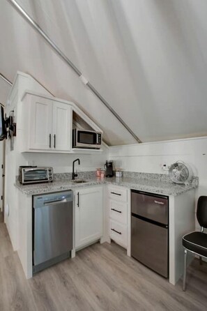 A compact kitchen with white cabinets, a microwave, a toaster, a dishwasher, and a refrigerator.
