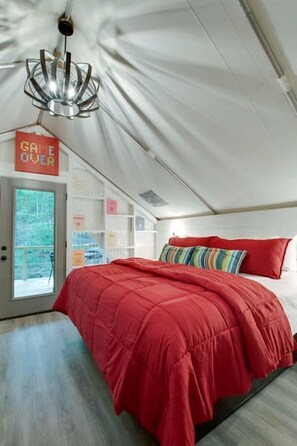 A bedroom with a red bedspread, a unique chandelier, and a view through a door.