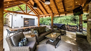 An outdoor covered patio with wooden beams, a dining table, chairs, a sofa, and a fan.