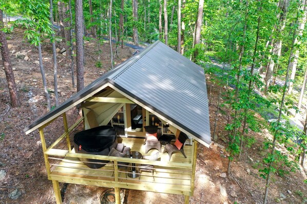 Une cabane en bois avec un toit en pente, une terrasse avec des sièges et un grand barbecue noir.