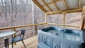 Ein Whirlpool auf einer Holzterrasse mit einem Metalltisch und Stuhl, umgeben von einem Metallgeländer, mit Blick auf einen Wald.