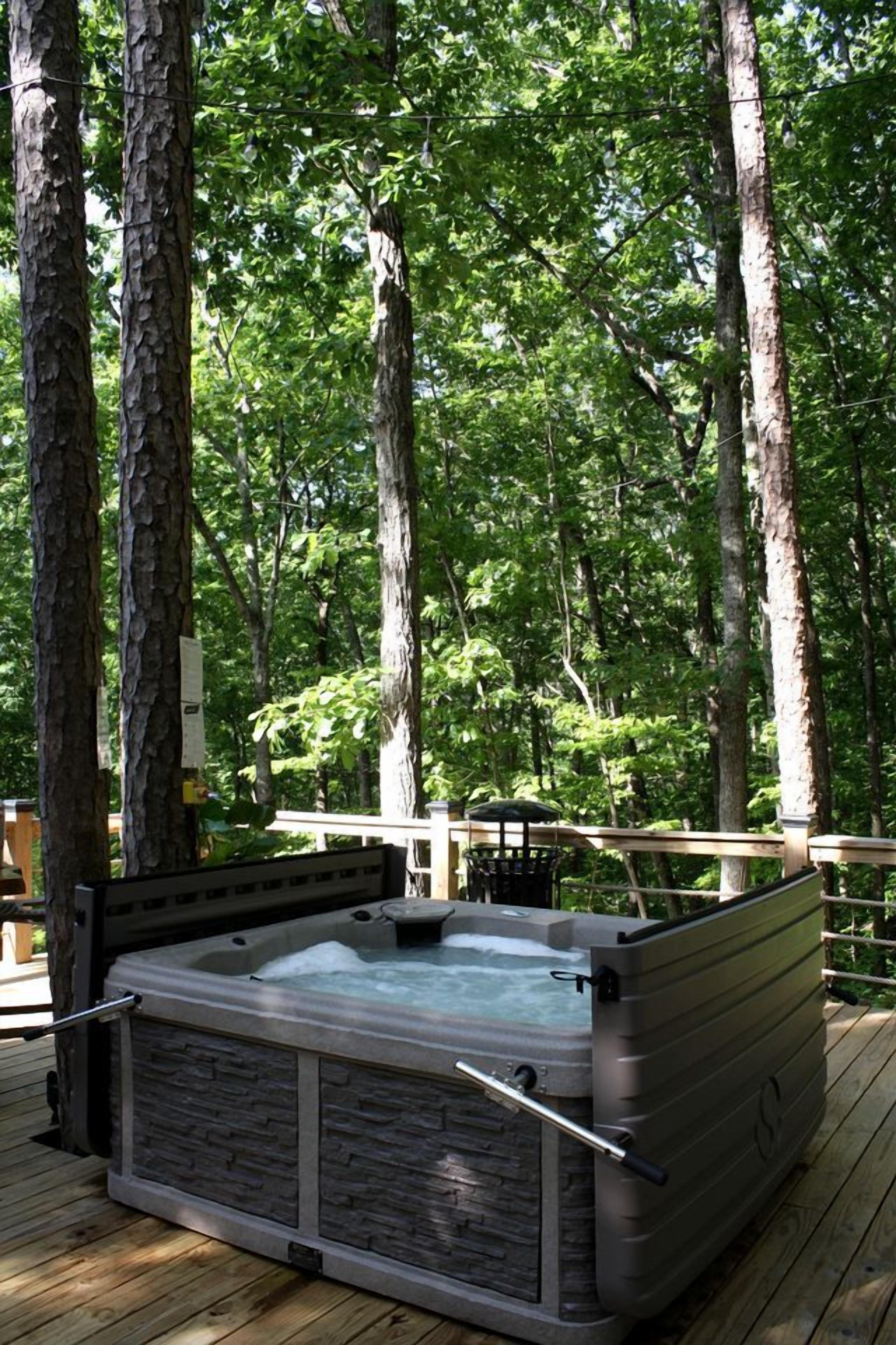 A hot tub on a wooden deck surrounded by trees.