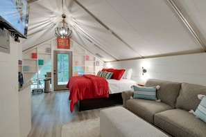 A cozy bedroom with a bed, a sofa, a TV, and a door leading outside.