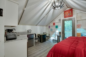 Um quarto tipo tenda com cozinha compacta, uma cama e um aviso com a mensagem 'GAME OVER'.