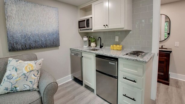 A modern kitchen with white cabinets, a granite countertop, stainless steel appliances, and a gray sofa with floral cushions.