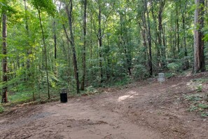 A forested area with a dirt path, a metal trash can, and a sign.